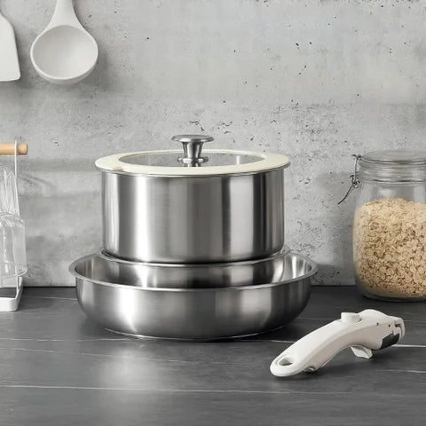 Set de poêles en inox empilées et la poignée devant sur fond gris