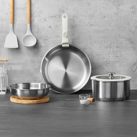 Set de poêles en acier inoxydables et leurs ustensiles sur fond gris