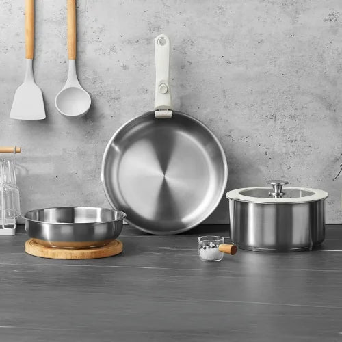 Set de poêles en acier inoxydables et leurs ustensiles sur fond gris