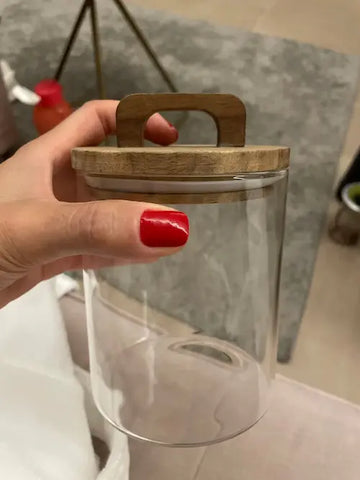 Une main tient un bocal en verre et bois