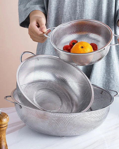 Trois passoires en inox, dont deux sûr une table et une entre deux mains