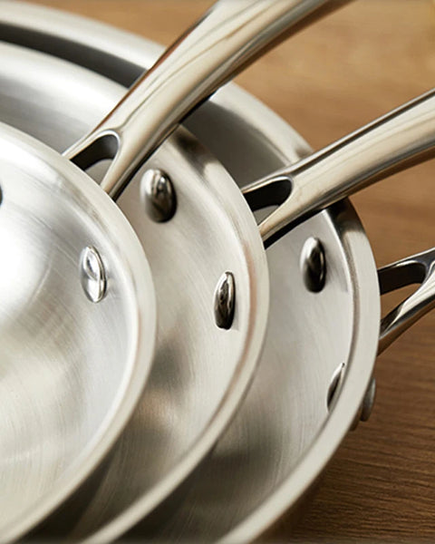 Trois Poêles en Inox empilées sûr un support en bois 